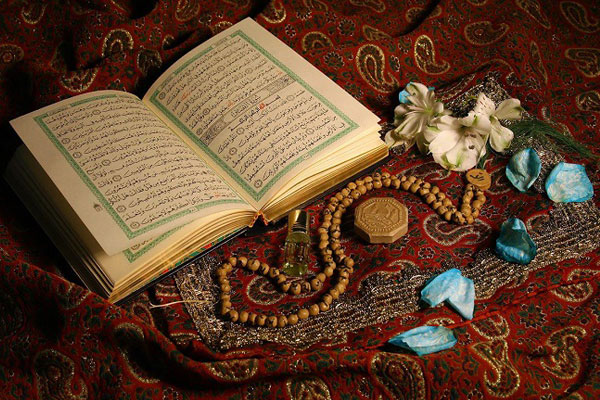 سجاده ای که بر روی آن مهر ، تسبیح ، قرآن و گل هایی قرار دارد